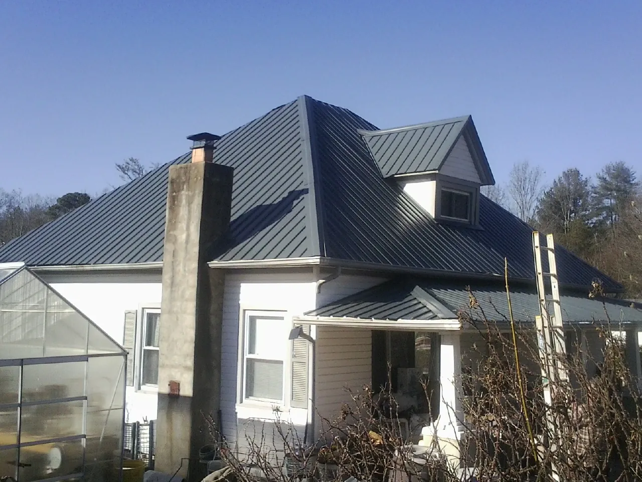 Dark blue standing seam metal roof on a white farmhouse with dormer — Slate & Tile Roof Repair by Roofing Brothers in Newman