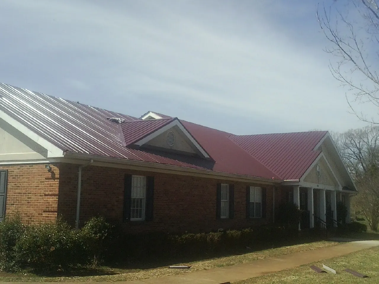 Red metal roof with gabled entries on a long brick building, from a Hail Damage Roof Repair job in Newman