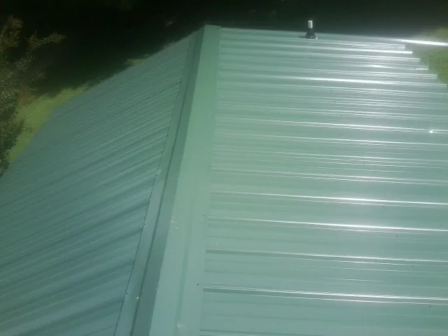 New green metal panels meeting at the ridge of a roof — Flat Roof Repair work by our crew in Newman