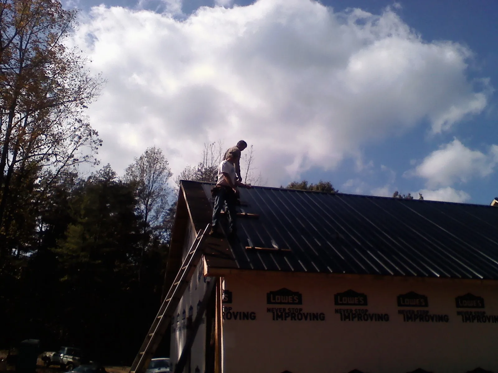 Roofer fastening dark metal panels high against a cloudy sky, from a Roof Inspection job in Newman