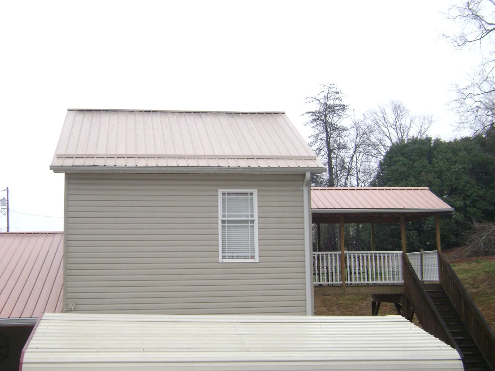 Tan metal roofs on a two story addition and attached porch, from a Roof Replacement job in Newman
